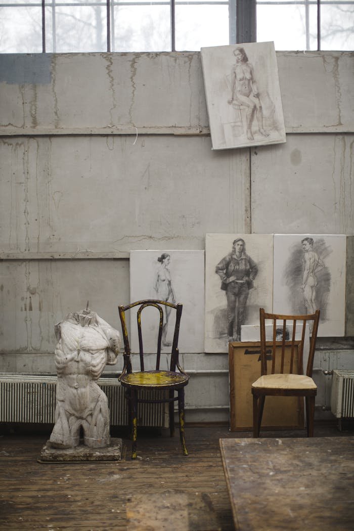 Interior view of an art studio featuring a Greek sculpture, chairs, and drawings.